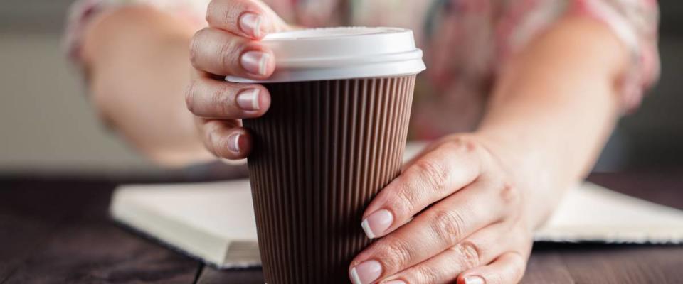 Woman holding takeout coffee at table and opening cup