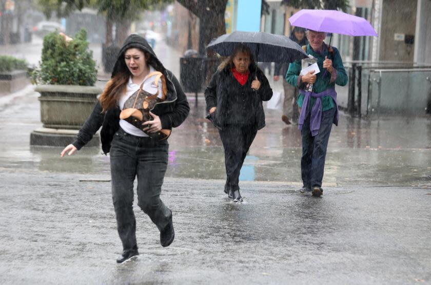 SANTA MONICA, CA - DECEMBER 20, 2023 - People make their way across Broadway during a morning downpour in Santa Monica on December 20, 2023. The first of two storm systems is bringing rain to parts of the Southland today, providing a preview of the second, more powerful system that forecasters say will give the region a more thorough dose of precipitation.(Genaro Molina/Los Angeles Times)