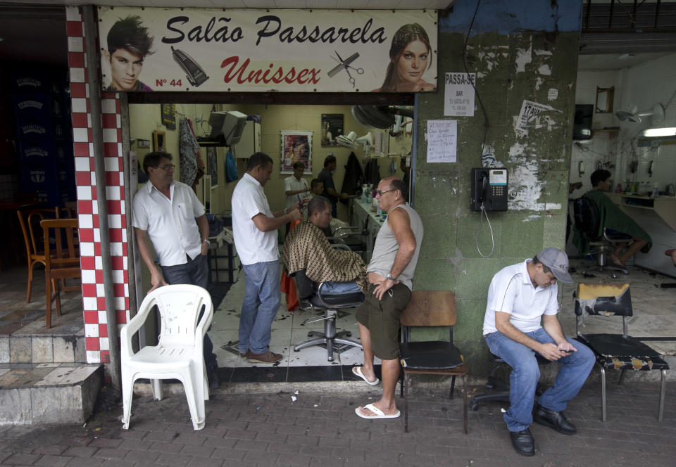 Residents get their hair cut at a hairdressing saloon in the Rocinha slum in Rio de Janeiro, Brazil, Monday, Feb.17, 2014. Police in Rio de Janeiro are reinforcing patrols in the Brazilian city's biggest slum after a weekend of shootouts. Rocinha is among Rio's "pacified" slums. In 2011, police entered and pushed the ruling drug gang out, and set up a permanent post. The slum pacification program is a key element of Rio's security plans ahead of this year's World Cup and the 2016 Olympics. (AP Photo/Silvia Izquierdo)