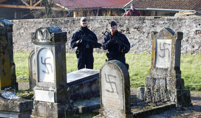 French police officers stand behind graves desecrated with swastikas at the Jewish cemetery in Westhoffen