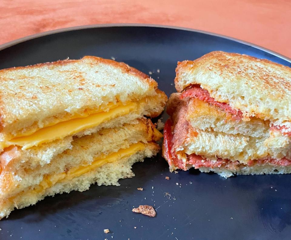 Grilled cheese sandwich cut in half on a plate, with melting cheese visible