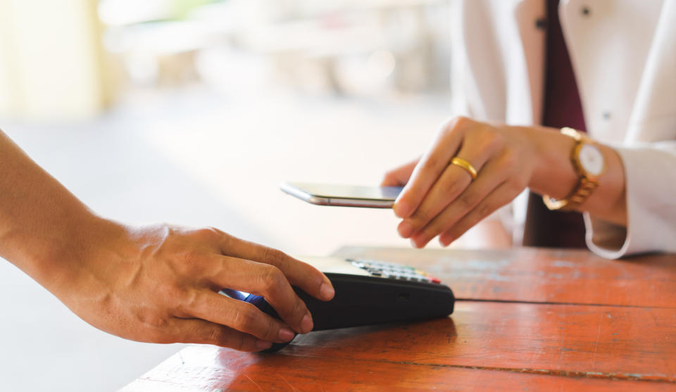 close up customer woman hand using smartphone for paying bill by using payment machine at table in the cafe , contactless payment concept