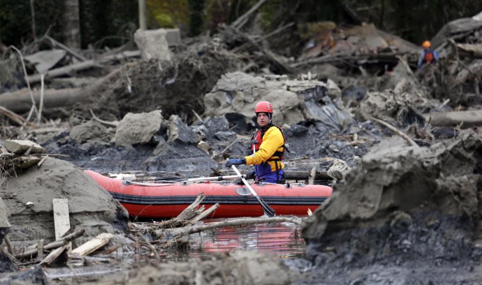 A searcher uses a small boat to look through debris from a deadly mudslide Tuesday, March 25, 2014, in Oso, Wash. At least 14 people were killed in the 1-square-mile slide that hit in a rural area about 55 miles northeast of Seattle on Saturday. Several people also were critically injured, and homes were destroyed. (AP Photo/Elaine Thompson)