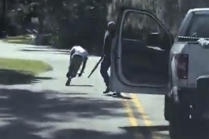 This image from video purports to show Ahmaud Arbery stumbling and falling to the ground after being shot as Travis McMichael stands by holding a shotgun.