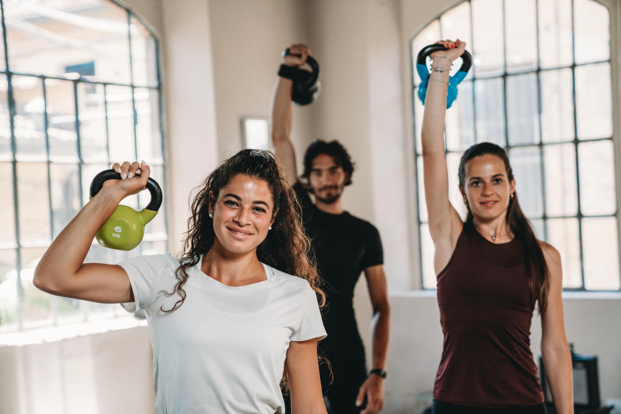 Three people at the health club are training together. They are using kettlebells.