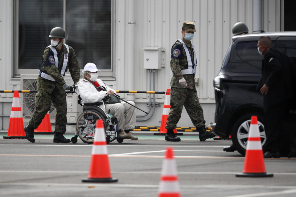 An unidentified passenger on a wheelchair is escorted after he disembarked from the quarantined Diamond Princess cruise ship Wednesday, Feb. 19, 2020, in Yokohama, near Tokyo. Passengers tested negative for COVID-19 started disembarking Wednesday. (AP Photo/Jae C. Hong)