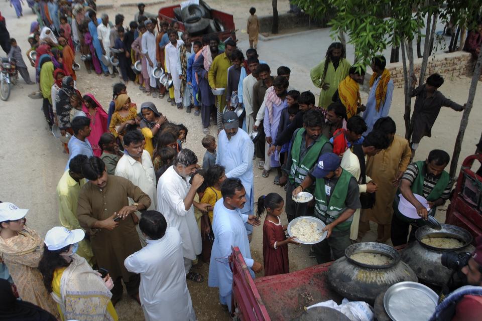 Volunteers from the Saylani Welfare Trust distribute food among flood-affected families, in Lal Bagh, Sindh province, Pakistan, Tuesday, Sept. 13, 2022. The death toll from three months of record-breaking floods in Pakistan rose to over 1,400 in rain-related incidents this week, officials said Tuesday, as the minister for climate warned the prolonged monsoon rains will continue lashing this impoverished nation in the coming weeks. (AP Photo/Pervez Masih)