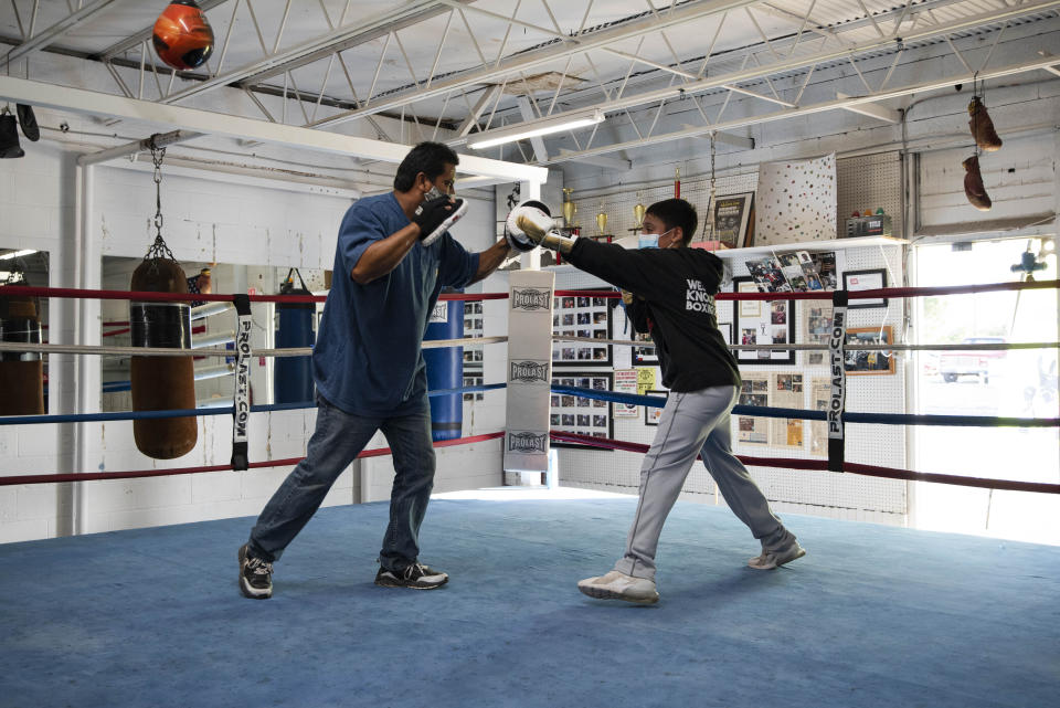 Coach Danny Chavez aids 14-year-old Estevan Rodriguez during boxing practice Tuesday, Aug. 4, 2020, at West Texas Knockout Boxing Club in Odessa, Texas. Both are wearing masks to abide by the boxing club's health and safety rules, to help prevent the spread of COVID-19. Tuesday was the club's first day open since late March. (Eli Hartman/Odessa American via AP)