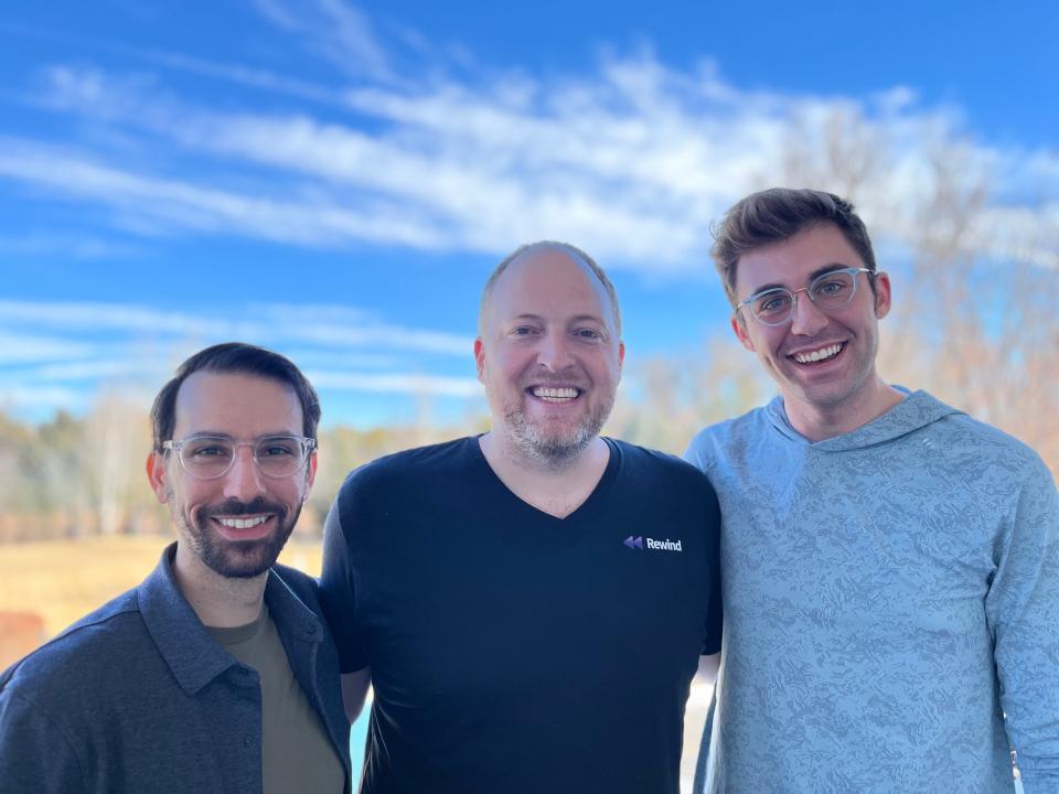 Three men standing next to each other in front of a landscape of trees and blue sky.