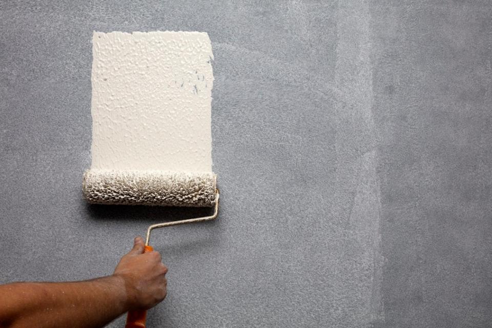 Person using paint roller to paint primer on a dark wall