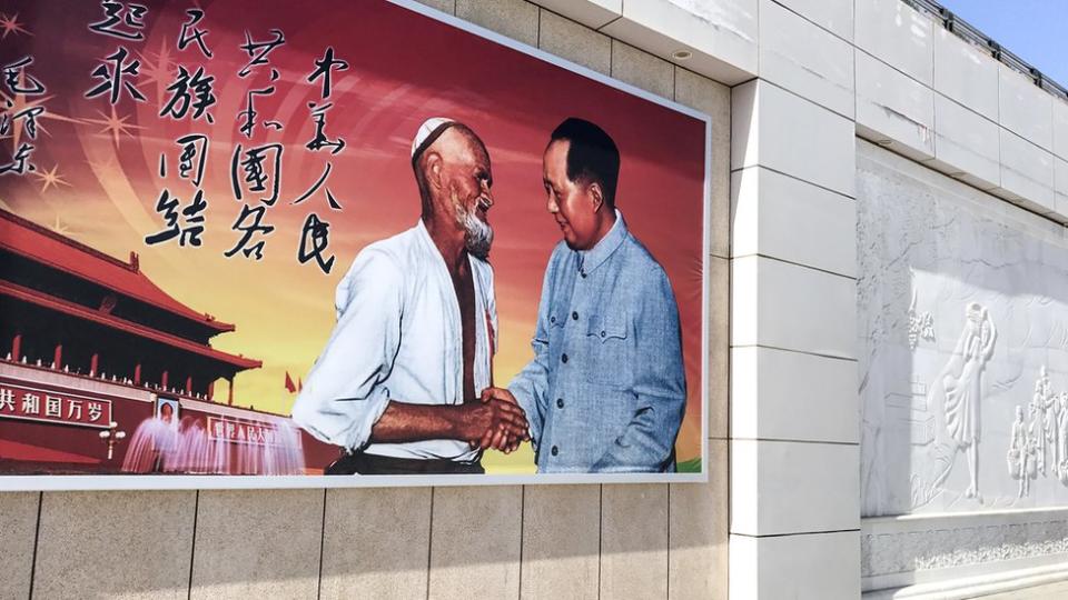 Cartel con una imagen de Mao Tse Tung dando la mano a un campesino uigur.