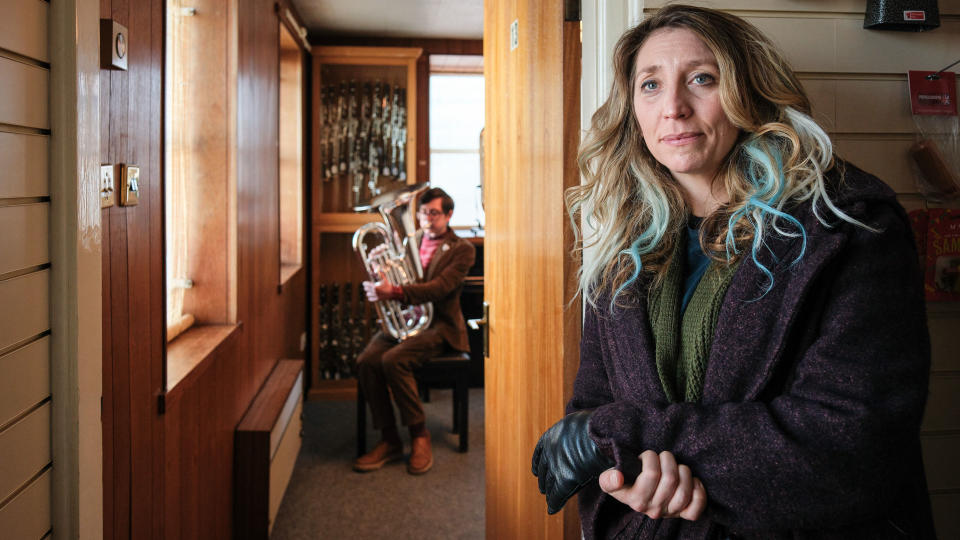 Alan holding a tuba with Janet in the foreground in Boat Story episode 3.