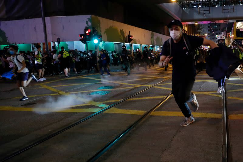 Pro-democracy demonstrators run away as riot police disperse them with pepper-spray pellet during a protest to mark first anniversary of a mass rally against a now-withdrawn extradition bill, in Hong Kong