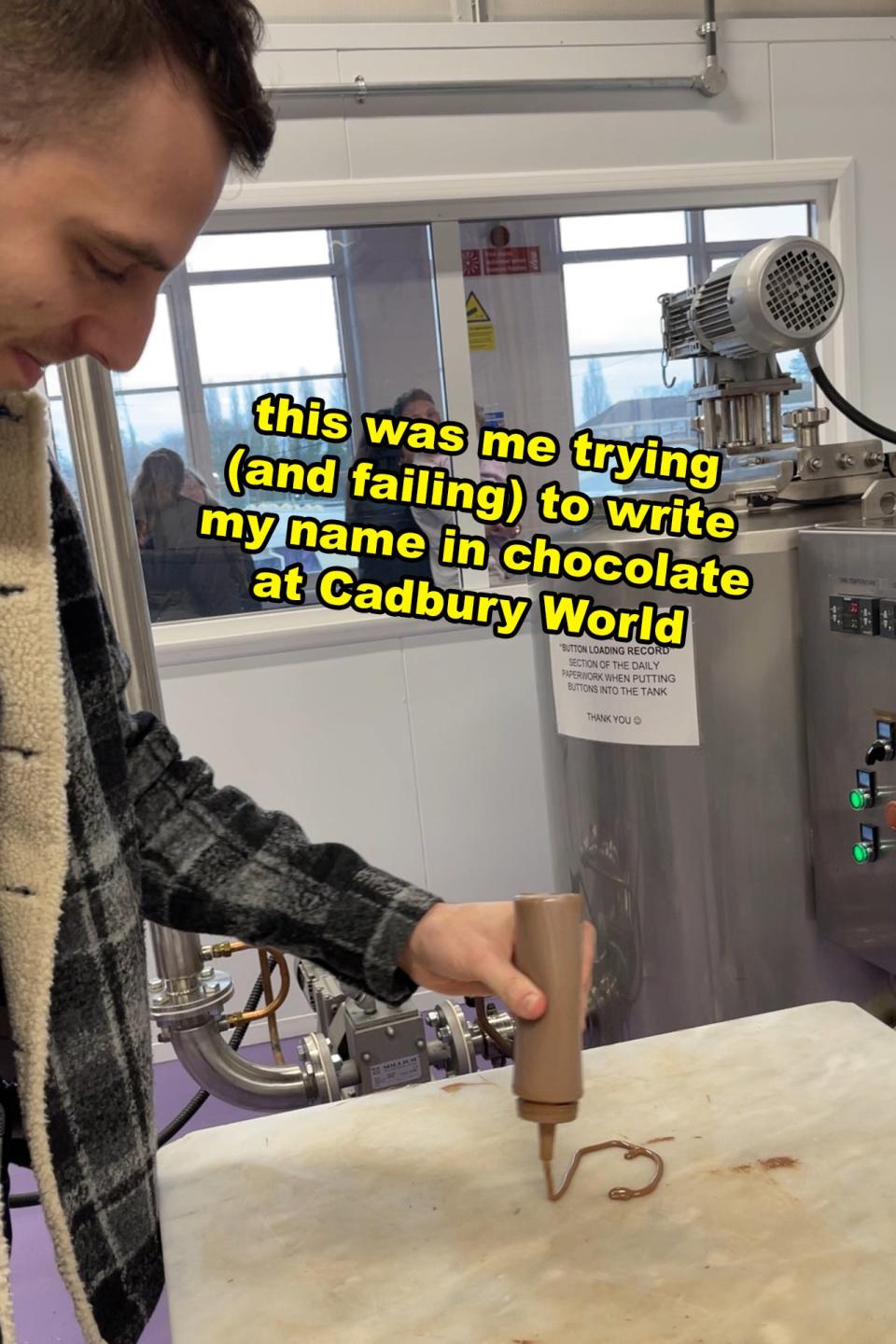 A person attempts to write their name in chocolate at Cadbury World. Text reads: 