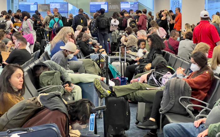 An airport lounge packed with passengers at close quarters, only a few wearing masks.