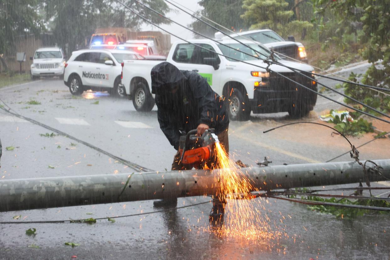 A worker cuts an electricity pole that was downed by Hurricane Fiona as it blocks a road in Cayey, Puerto Rico, Sunday, Sept. 18, 2022.