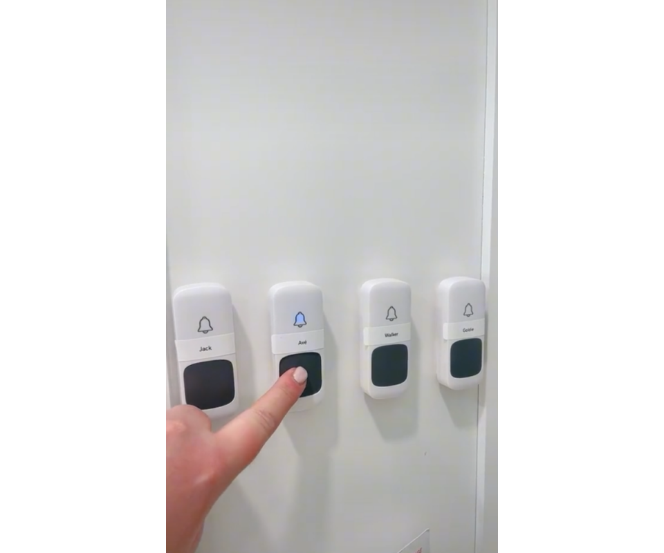 A caucasian woman's finger reaches to touch one of our white doorbell buttons on the inside of a white pantry.