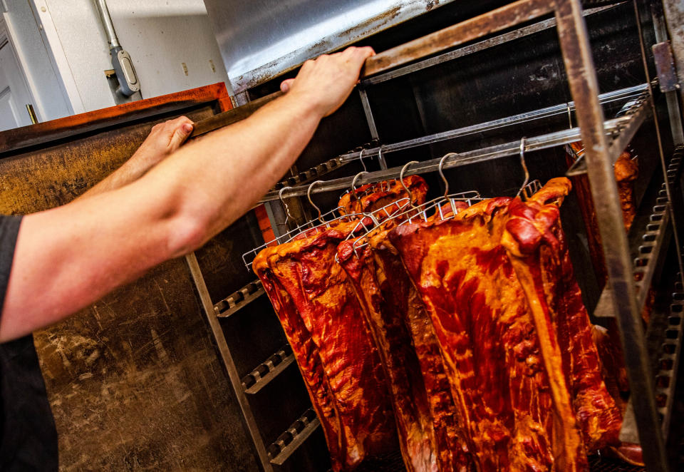 Casey Weber, owner of Tallgrass Meat Co., pulls out racks of freshly smoked meats to prepare them for packaging and display on July 18, 2022.