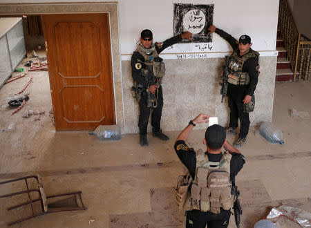 Iraqi special forces soldiers pose for a photograph in front of a Islamic States drawing inside a building located inside a church compound in Bartella, east of Mosul, Iraq October 21, 2016. REUTERS/Goran Tomasevic