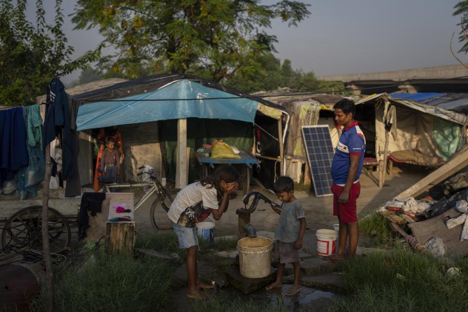 Shiv Kumar, right, watches as his eldest daughter Garima, 10, left, washes her face and his son Kartik, 4, brushes his teeth outside their shanti on the flood plain of Yamuna River, in New Delhi, India, Friday, Sept. 29, 2023. (AP Photo/Altaf Qadri)