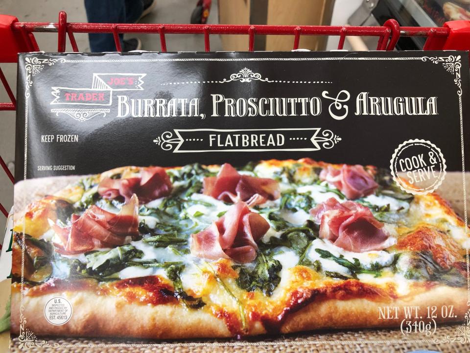 A box of Trader Joe's burrata, prosciutto, and arugula flatbread in a red shopping cart.