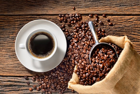 A coffee cup and coffee beans sitting on a table.