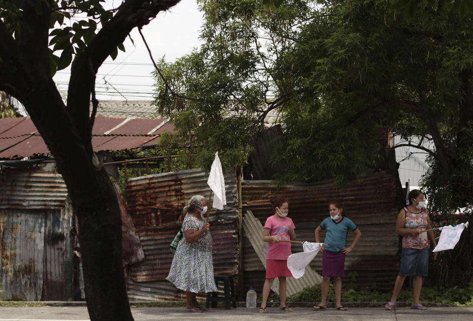 Una familia levanta banderas blancas para pedir comida a los autos que pasan por la Carretera de Oro en Ilopango, El Salvador, el martes 19 de mayo de 2020. (AP Foto/Salvador Melendez)