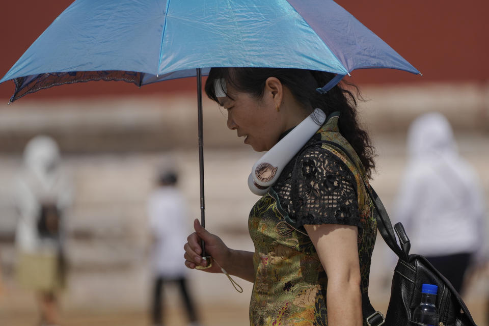 A woman wearing an electric fan and carrying an umbrella visits the Forbidden City on a sweltering day in Beijing, Friday, July 7, 2023. Earth's average temperature set a new unofficial record high on Thursday, the third such milestone in a week that already rated as the hottest on record. (AP Photo/Andy Wong)