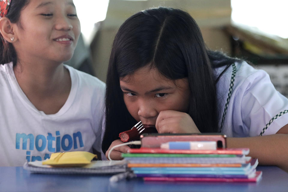 Grade school student Bhea Joy Roxas, right, grabs a quick bite during an online class using a nearby store's wifi connection inside a passenger jeepney at the Tandang Sora jeepney terminal in Quezon city, Philippines Monday, Oct. 5, 2020. Grade and high school students in the Philippines have started classes at home after the pandemic forced remote-learning onto an educational system already struggling to fund schools.(AP Photo/Aaron Favila)