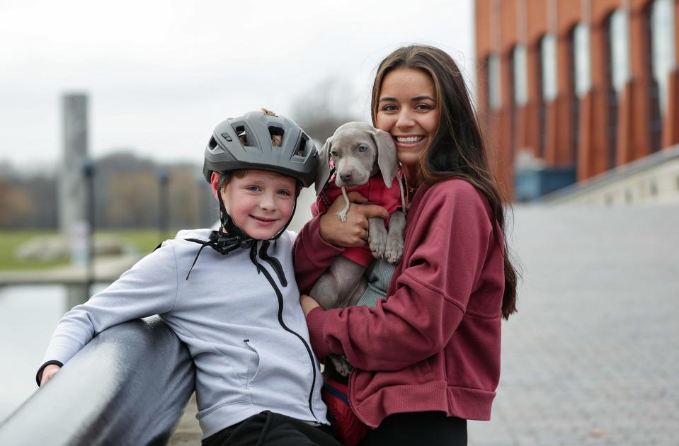 Paige Bramlett first met and bonded with her 7-year-old son William while working as his behavior specialist at school in Johnson County in 2019. She began fostering him shortly after and finally adopted William in October 2021. A video of William receiving a puppy for Christmas recently went viral on TikTok, leading the family to appear on Good Morning  America and in People Magazine. Pictured, Paige Bramlett poses with William and their puppy Banks on Thursday, Dec. 30, 2021, at White River State Park in Indianapolis.