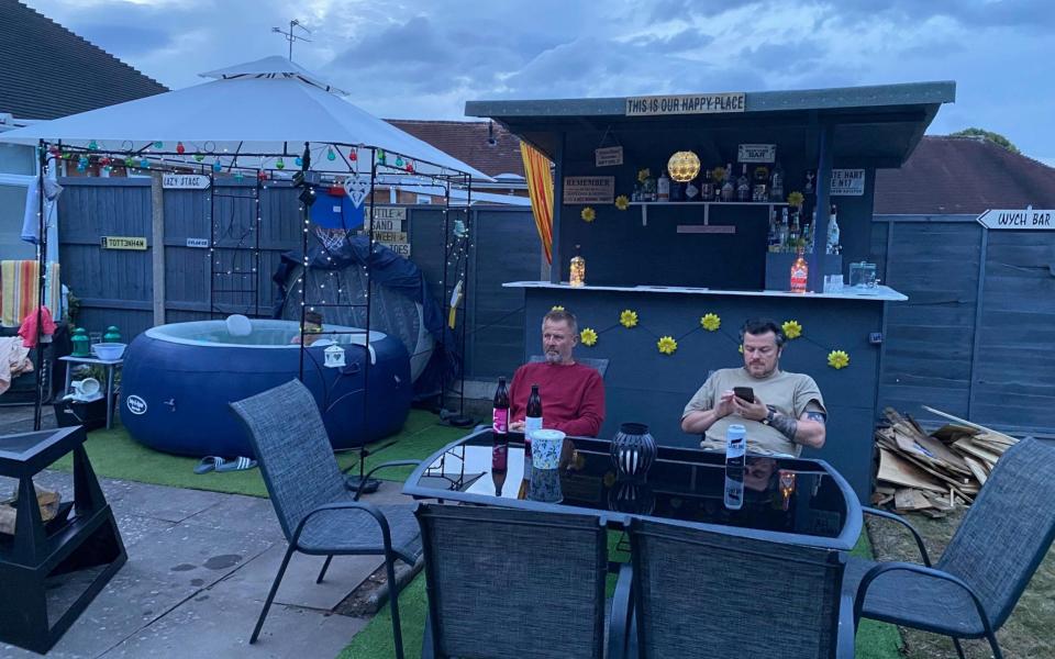 Two men sit at table at back garden Glastonbury - Fiona Rees/PA