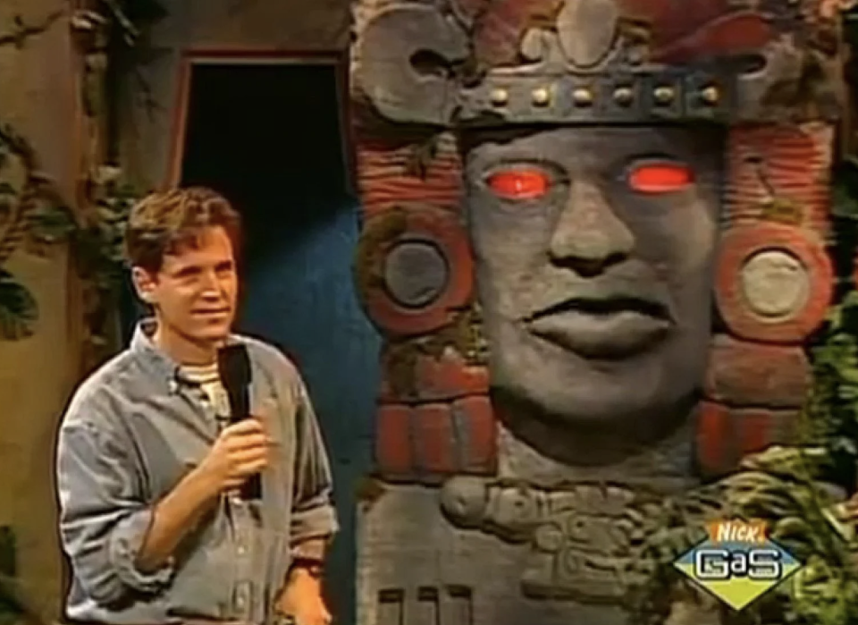 Olmec statue behind a host with a microphone