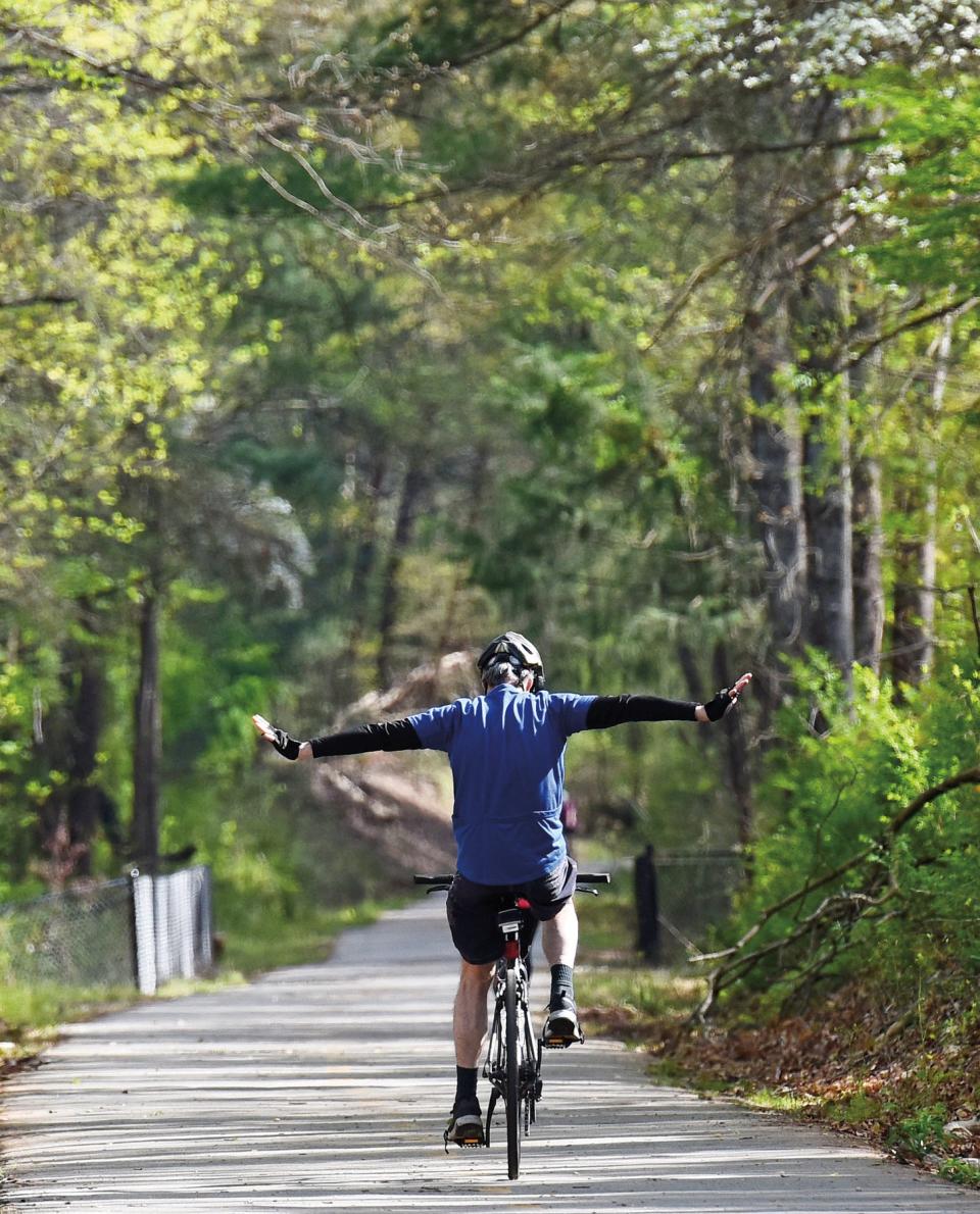 A cyclist stretches his arms out while riding down the Swamp Rabbit Trail near Furman University.