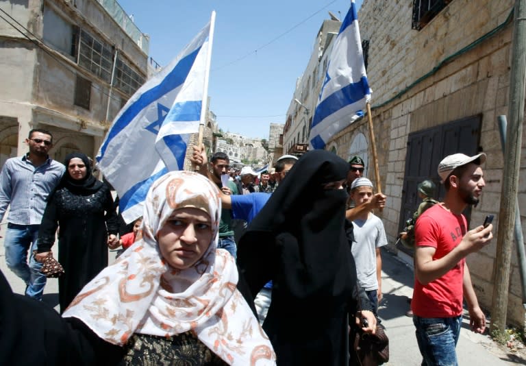 A group of Israeli settlers (back) are guarded by soldiers and border police as they march through the West Bank city of Hebron, on July 1, 2016