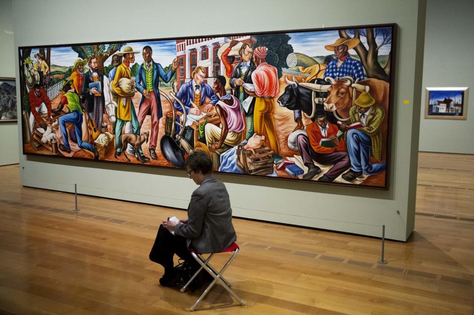 In this Monday, Feb. 6, 2017 photo, Hale Woodruff's 1942 painting "Opening Day at Talladega College," is displayed as a docent takes notes during a tour of the exhibit "Cross Country: The Power of Place in American Art, 1915-1950," at the High Museum of Art in Atlanta. The new exhibition at takes a look at how American artists during the modernist period traveled outside cities to find inspiration in the rural landscape. (AP Photo/David Goldman)