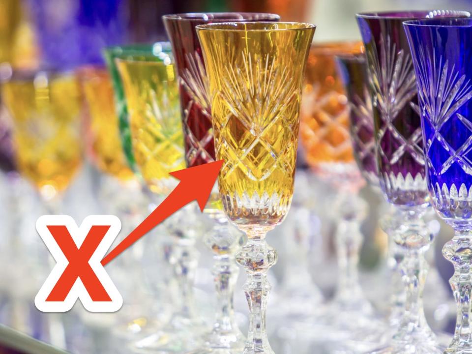Blue, red, green, and yellow crystal champagne flutes on shelf with red X and arrowing pointing to glasses