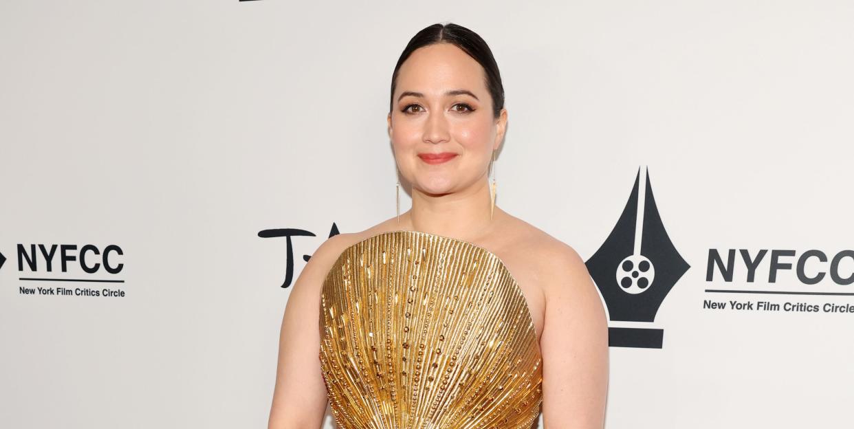 lily gladstone smiles on the red carpet in a strapless gold floor length dress