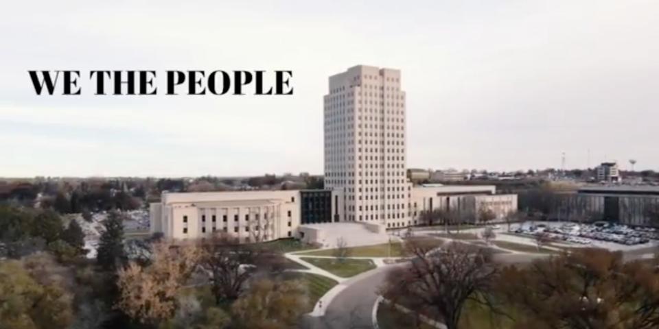 A video still showing the North Dakota State Capitol from the air, superimposed with the text 'We The People.'