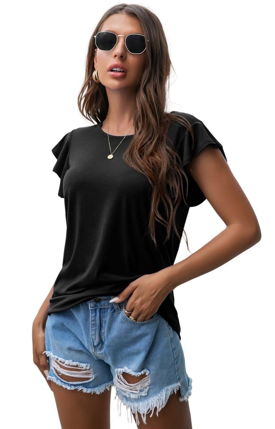 model wearing sunglasses, a black top with ruffle sleeves tucked into distressed denim shorts