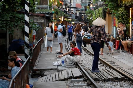 A woman sits on a railway track as tourists gather along it on a street in the Old Quarter of Hanoi, Vietnam