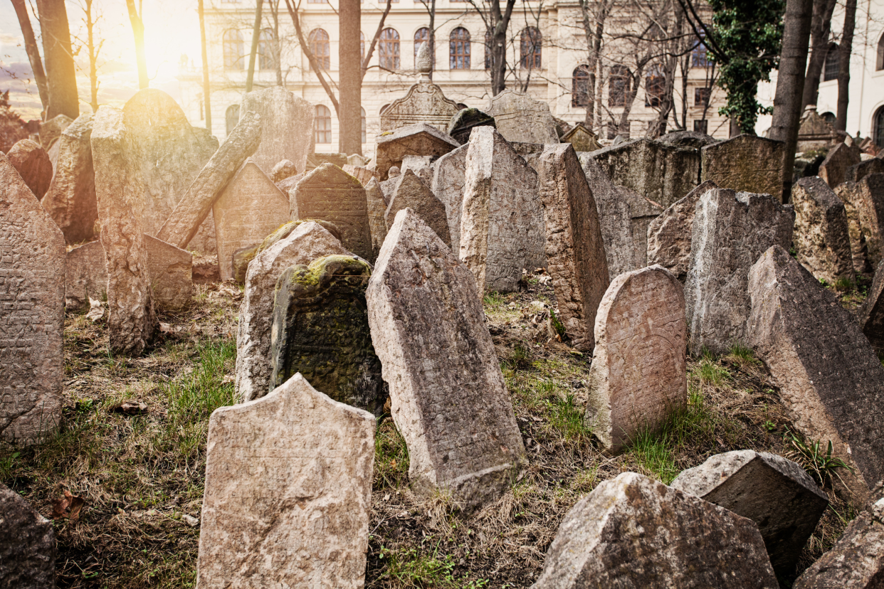 Old Jewish Cemetery, Prague, Czech Republic, several jumbled headstones with the sunlight coming through the bare trees in winter with buildings in the background