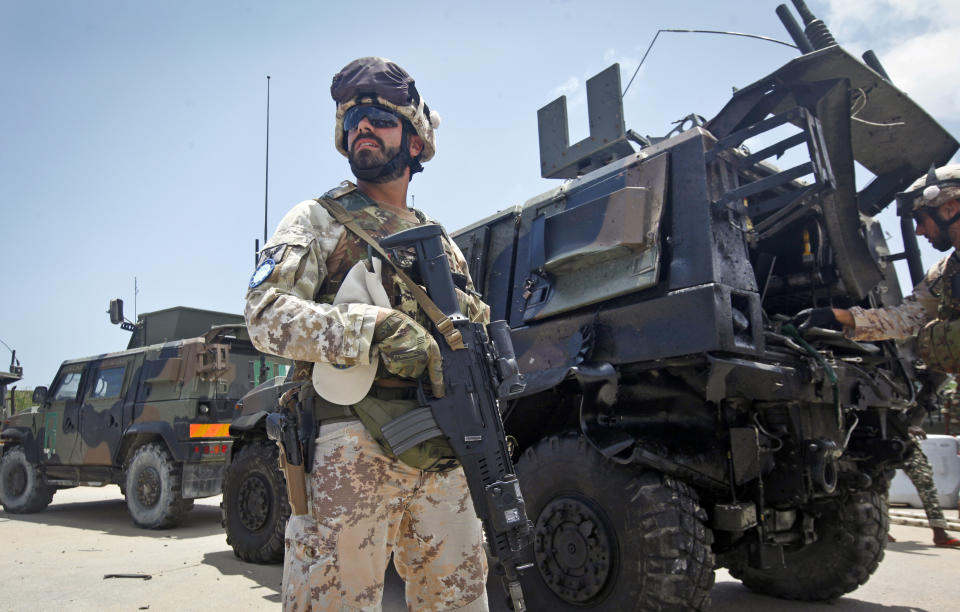 A member of the Italian military stands guard at the scene next to a damaged armored personnel carrier after an attack on a European Union military convoy in the capital Mogadishu, Somalia Monday, Oct. 1, 2018. (AP Photo/Farah Abdi Warsameh)