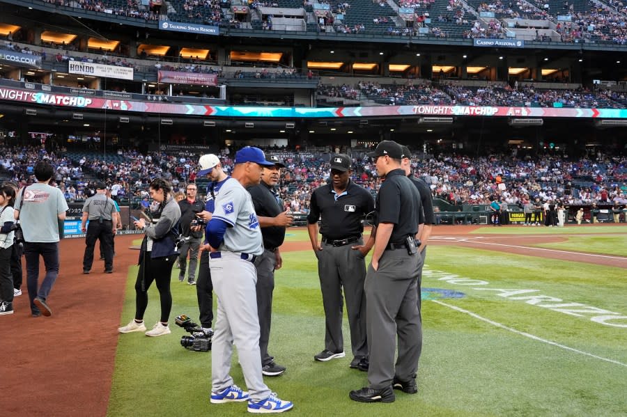 Los Angeles Dodgers manager Dave Roberts, left, talks with the umpires regarding a swarm of bees gathered on the net behind home plate delaying the start of a baseball game against the Arizona Diamondbacks, Tuesday, April 30, 2024, in Phoenix. (AP Photo/Matt York)