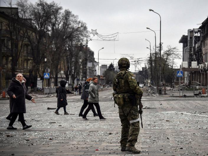People pass by a Russian soldier in central Mariupol on April 12, 2022.