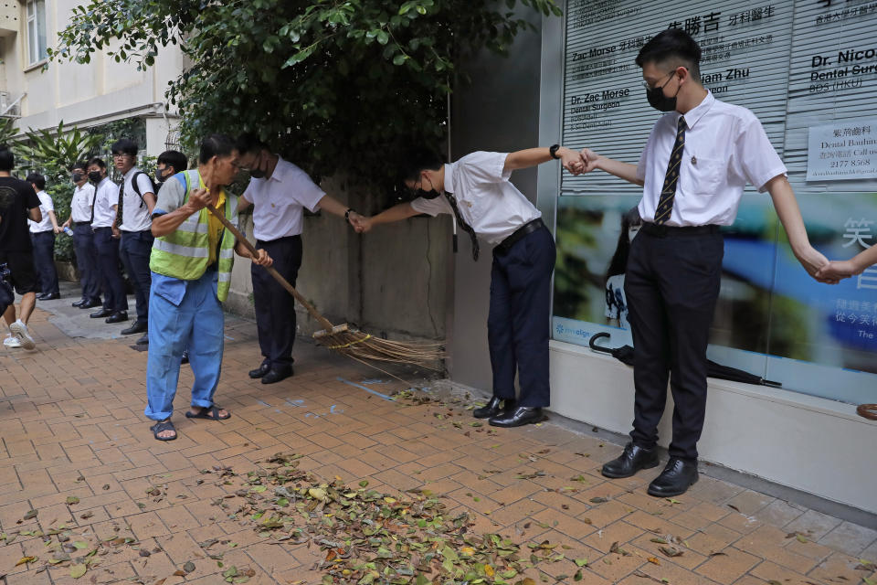 A worker sweeps a road as students hold hands to surround St. Paul's College in Hong Kong, Monday, Sept. 9, 2019. Thousands of demonstrators in Hong Kong urged President Donald Trump to "liberate" the semiautonomous Chinese territory during a peaceful march to the U.S. Consulate on Sunday, but violence broke out later in the business and retail district as police fired tear gas after protesters vandalized subway stations, set fires and blocked traffic. (AP Photo/Kin Cheung)
