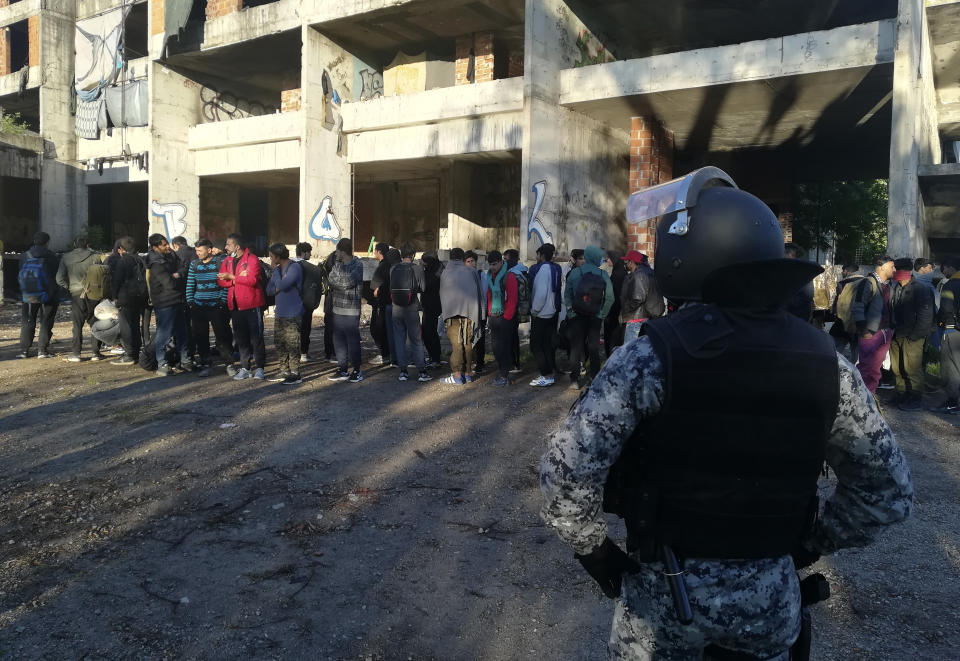 Bosnian police officers guard migrants as they leave to be relocated from an abandoned building in Bihac, northwestern Bosnia, Tuesday, May 18, 2021. Bosnian police have rounded up over 200 migrants who were squatting in an abandoned building in a northern town in order to move them to a nearby tent camp. (AP Photo/Hasan Arnautovic)