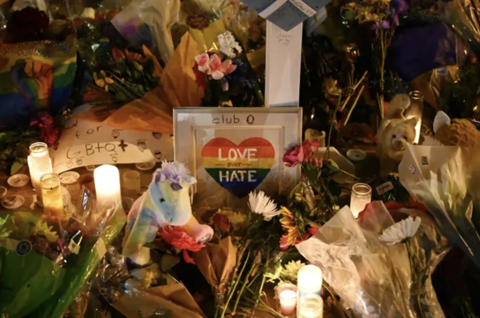 A memorial with flowers and candles and a small photo frame that says "love over hate" in a rainbow heart