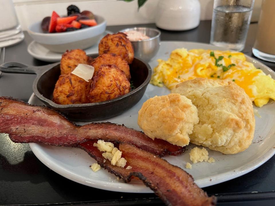 A plate with hashbrowns, bacon, eggs, and a biscuit on it.