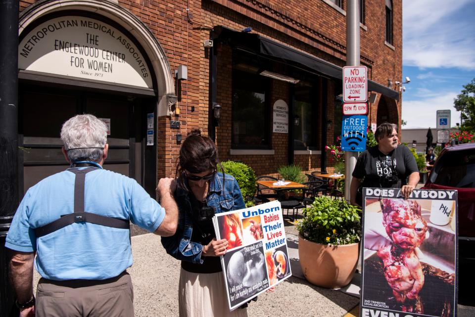 (From left) Randy and Rachel (would not give last names) pray as they protest in front of The Englewood Center For Women on Saturday, June 18, 2022. (Right) Robert (would not give last name) holds a sign. 
