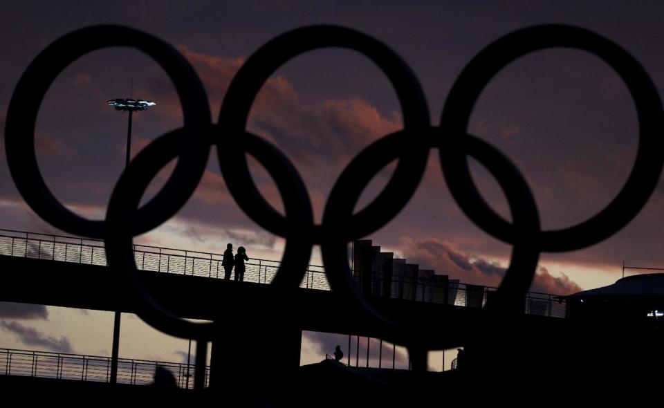 Two people stand on a bridge with the Olympic rings in the foreground at sunset ahead of the 2014 Winter Olympics, Wednesday, Feb. 5, 2014, in Sochi, Russia. (AP Photo/Julio Cortez)